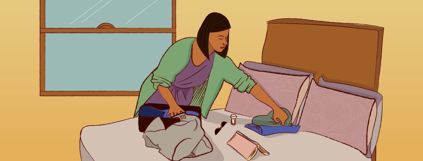 A woman leans over her open suitcase on a bed, packing comfy clothes, medication, sunglasses, and a notebook.